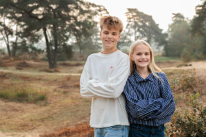 Jesse en Isa staan samen in het landschap en kijken lachend naar de camera. De bomen en heide op de achtergrond geven de foto een rustige, natuurlijke uitstraling.