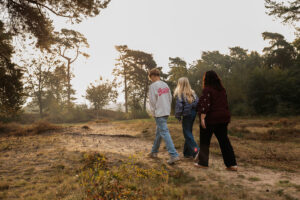 Jesse, Isa en hun moeder lopen samen over het zandpad terwijl het warme zonlicht tussen de bomen door valt. Een spontaan moment tijdens hun familiefotoshoot.