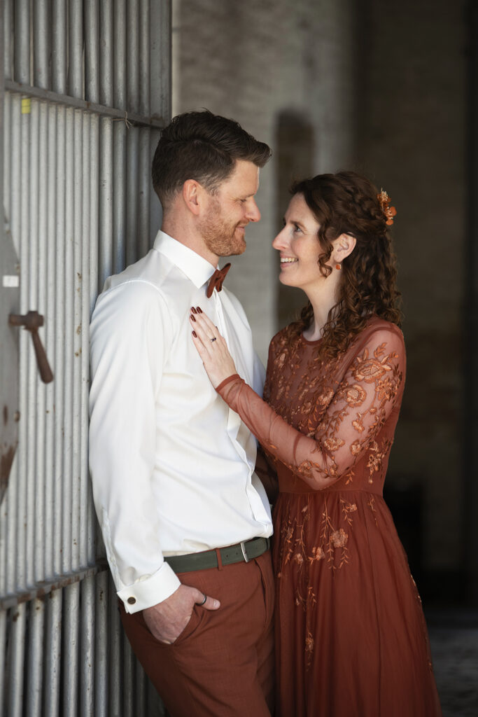 Bruid en bruidegom kijken elkaar verliefd aan terwijl ze samen poseren tegen een poort in de Blokhuispoort.