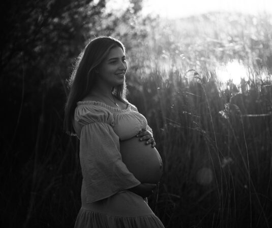 Zwangere vrouw in zwart-wit, staand in het veld bij zonlicht