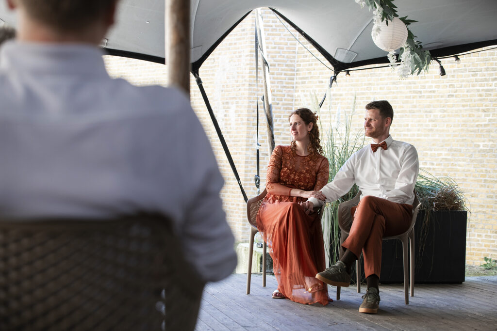 Het bruidspaar zit hand in hand op stoelen en luistert aandachtig tijdens de ceremonie.