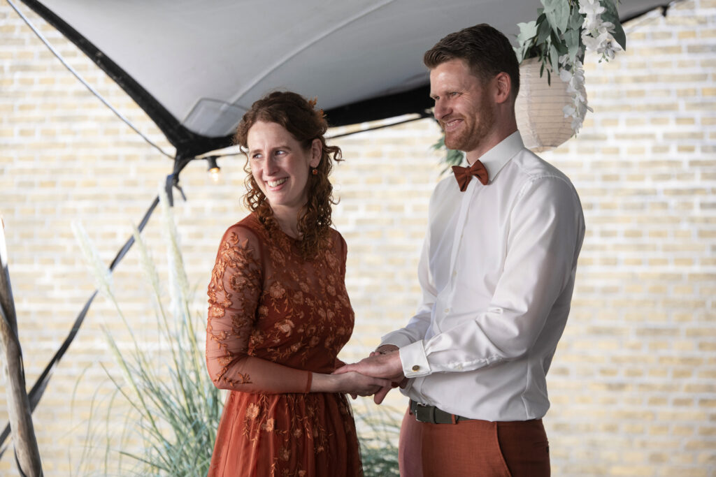 Het bruidspaar staat hand in hand en lacht liefdevol tijdens het uitspreken van hun geloften.