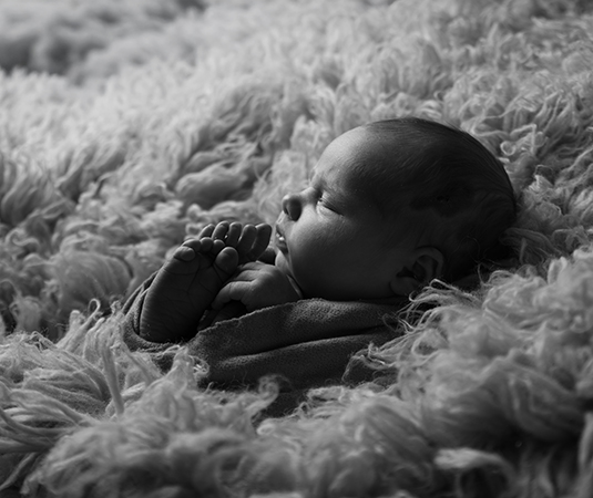 Zwart-wit newbornfoto van een slapende baby op een zachte, wollen ondergrond, vastgelegd in rustige zijligging.