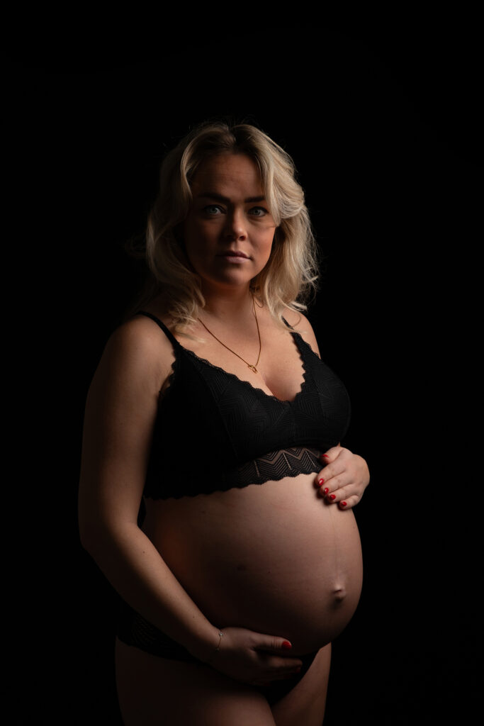 Portret van een zwangere vrouw in zwarte lingerie tijdens een studio zwangerschapsshoot in Leeuwarden met dramatisch licht en warme tinten.