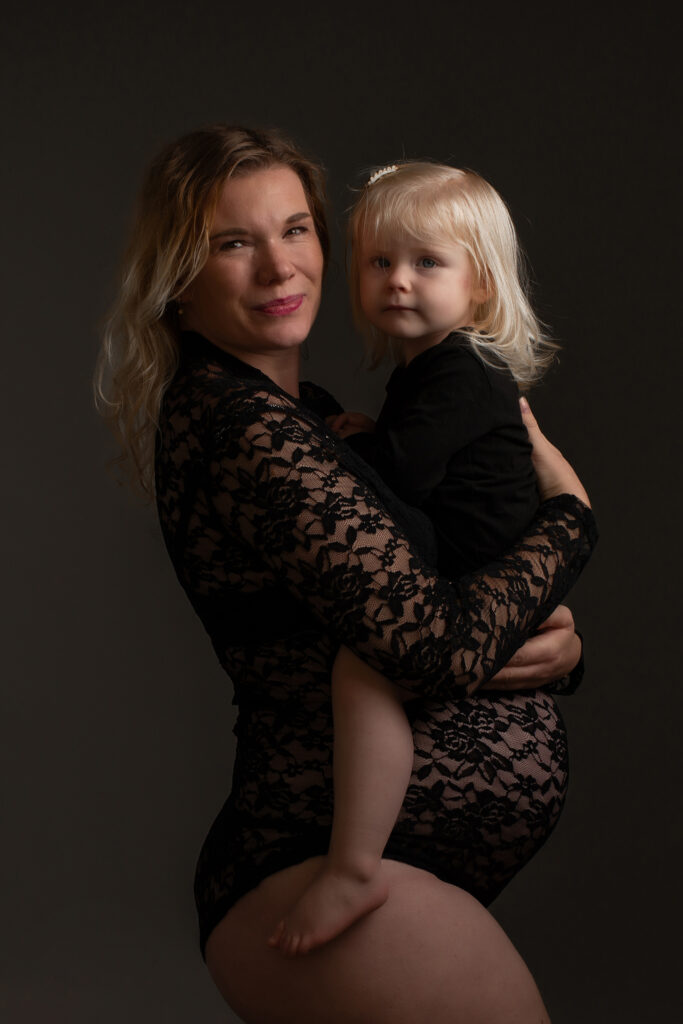 Zwangere moeder houdt haar peuterdochter in de armen tijdens zwangerschapsshoot in studio Leeuwarden.