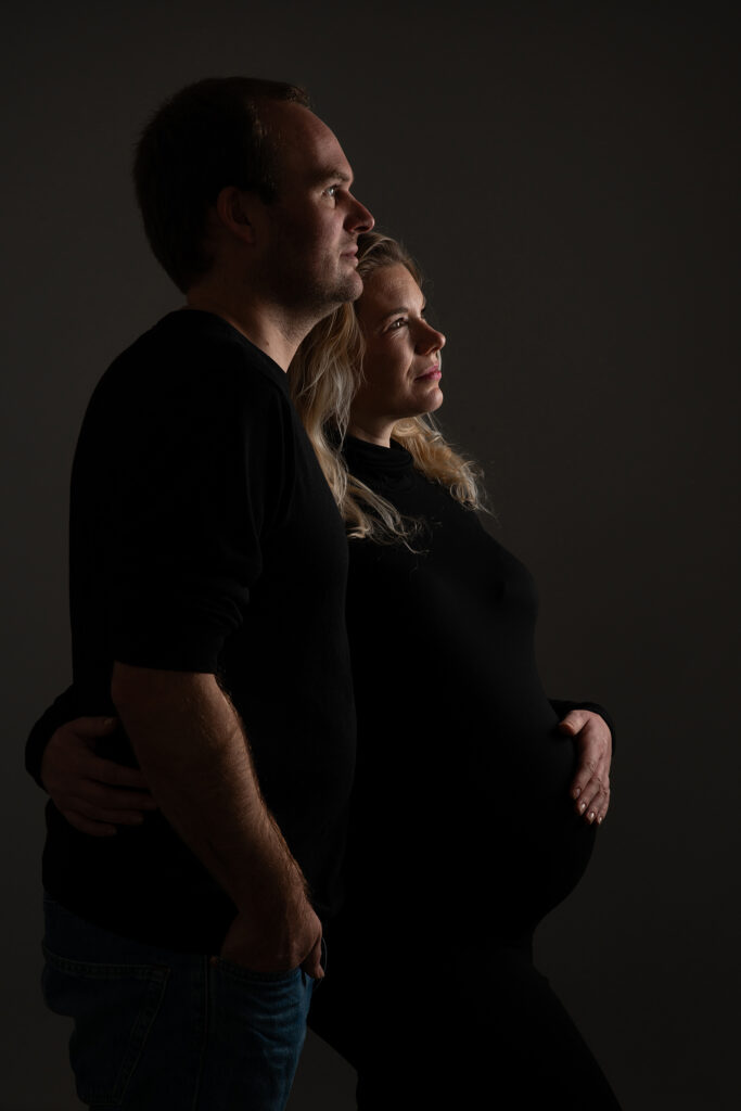 Zwangere vrouw met haar partner tijdens intieme studioshoot in Leeuwarden, beiden in zwart gekleed.