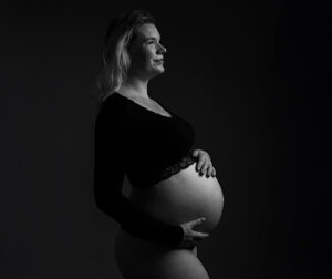 Zwangere vrouw in zwarte crop top poseert krachtig in zwart-wit tijdens zwangerschaps shoot.