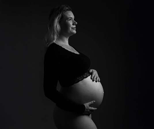 Zwangere vrouw in zwarte crop top poseert krachtig in zwart-wit tijdens zwangerschaps shoot.
