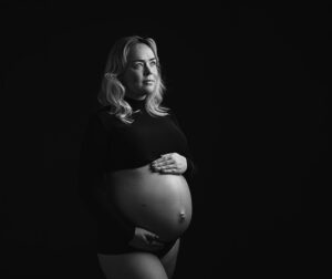 Zwart-wit portret van een zwangere vrouw in studio tijdens zwangerschapsshoot in Leeuwarden met minimalistische belichting.