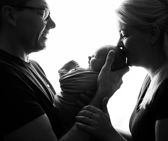 Zwart-wit newbornfoto van ouders die hun pasgeboren baby liefdevol vasthouden in de studio