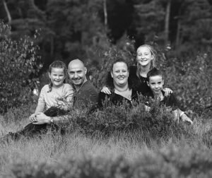Familiefoto in zwart-wit van gezin met drie kinderen, zittend in de heide tijdens een fotoshoot in Bakkeveen