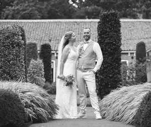 Het bruidspaar poseert samen in een prachtige tuin in Leeuwarden, de bruid lachend naar haar bruidegom terwijl ze hand in hand staan tussen weelderige groene struiken en zorgvuldig gesnoeide heggen.