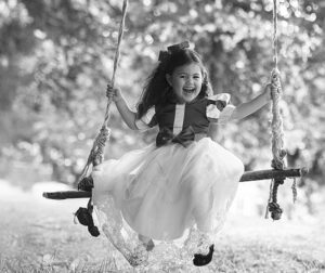 Lachend meisje in Sneeuwwitje-jurk op houten schommel in zwart-wit foto