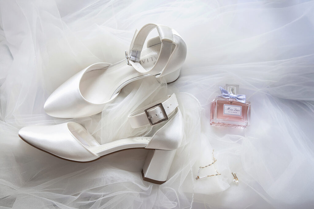 Close-up van witte bruidsschoenen, Miss Dior parfum en sieraden tijdens trouwdag in Friesland
