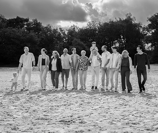 Zwart wit foto van een grote familie die loopt gezamenlijk op de bakkeveense duinen tijdens een fotoshoot en hebben plezier.