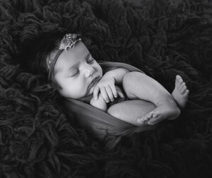 Pasgeboren meisje slaapt rustig in een zachte wrap op een donkere fluffy ondergrond tijdens een newbornshoot in aardetinten.