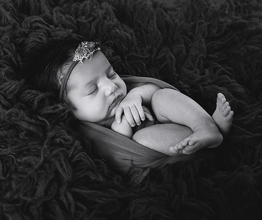 Pasgeboren meisje slaapt rustig in een zachte wrap op een donkere fluffy ondergrond tijdens een newbornshoot in aardetinten.