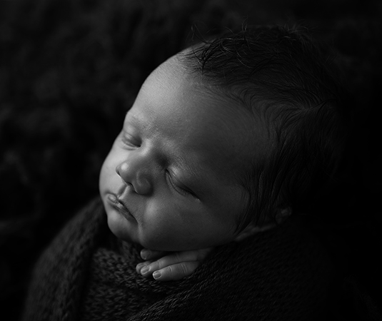Een close-upfoto van een slapende pasgeboren baby, ingewikkeld in een zachte, donkere wikkel