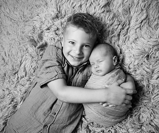 Grote broer Wolf geeft zijn pasgeboren broertje Scott een liefdevolle knuffel tijdens een newbornshoot in Leeuwarden.