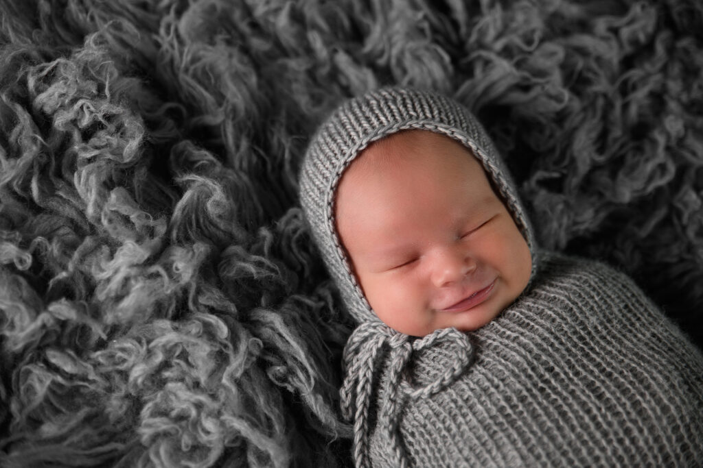 Pasgeboren baby Scott slaapt tevreden in een grijze gebreide wrap op een donkergrijze wollen achtergrond tijdens een newbornshoot in Leeuwarden.