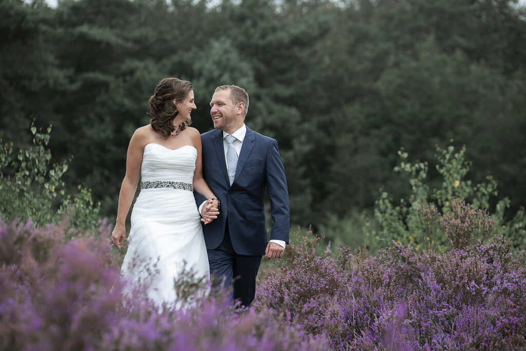 Intiem moment tussen koppel in trouwkleding tijdens jubileum fotoshoot op heide.