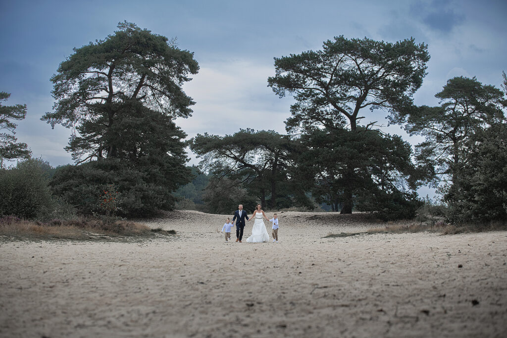 Een intieme gezinsfoto van het koppel met hun zoons, Tiemen en Melle, tijdens een jubileum fotoshoot op de bloeiende heide in Bakkeveen. De familie straalt geluk en liefde uit.