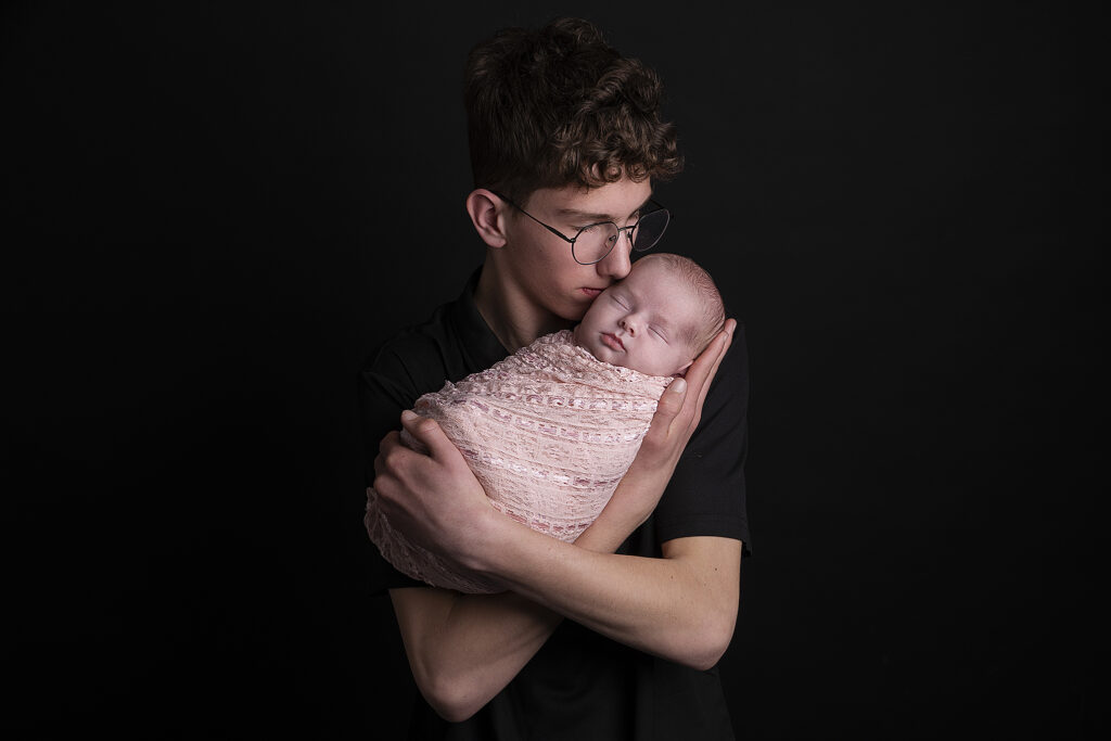 Grote broer houdt liefdevol zijn slapende pasgeboren zusje vast tijdens een newbornshoot in Friesland.