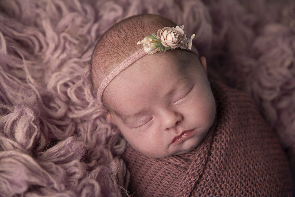 Close-up van een slapend pasgeboren meisje met bloemenhaarbandje tijdens een newborn fotoshoot in Leeuwarden.