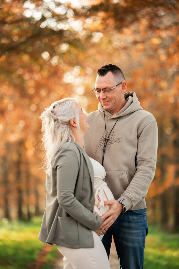 Michelle en haar partner staan samen in een prachtig herfstdecor in Leeuwarden. De warme tinten van het bladerdek vormen een zachte achtergrond terwijl zij liefdevol haar buik vasthouden. Een intiem en warm moment tijdens de zwangerschapsshoot.