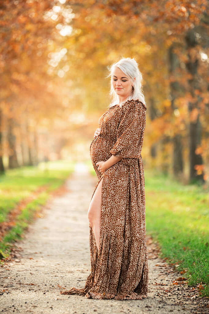 Michelle draagt een stijlvolle, soepel vallende bruine jurk uit de client closet. De herfsttinten in het natuurgebied sluiten perfect aan bij haar look. Een elegante en tijdloze zwangerschapsfoto op een van de mooiste locaties in Leeuwarden.