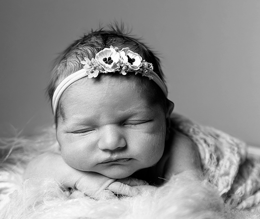 Zwart-wit close-up van slapende newborn met bloemenhaarband tijdens een newbornshoot in Leeuwarden.