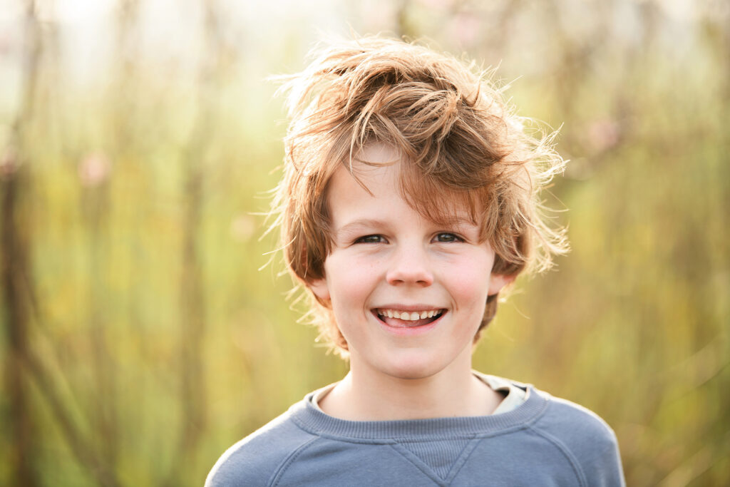 Jongen met warrig haar glimlacht tijdens een fotoshoot op het erf van Boer Bart