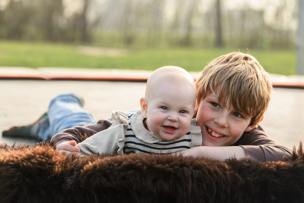 Jongen ligt op trampoline met zijn baby zusje tijdens een gezinsfotoshoot