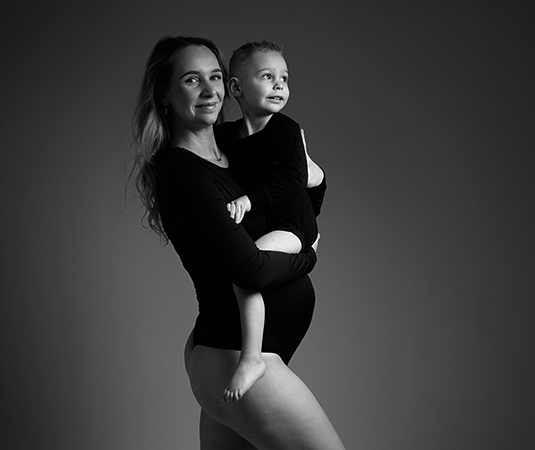 Tijdloze zwart wit foto. Moeder is zwanger en glimlacht naar de camera. Ze poseert met haar zoon in haar armen.