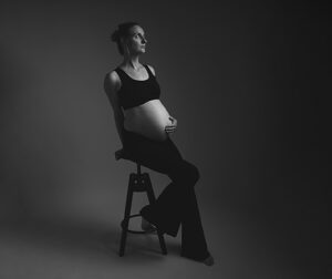 Zwart-wit portret van een zwangere vrouw op een kruk tijdens een fine art zwangerschapsshoot.