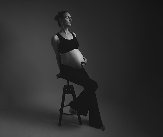 Zwart-wit portret van een zwangere vrouw op een kruk tijdens een fine art zwangerschapsshoot.