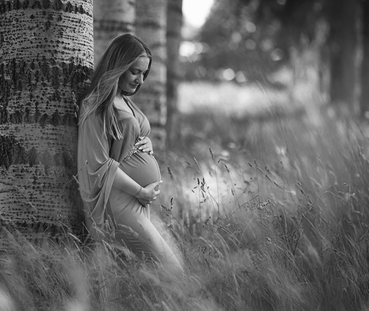 Zwangere vrouw in zwart-wit beeld leunt tegen boom in natuurlijk landschap